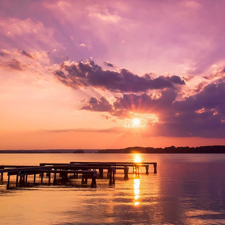 Sunset over a lake with clouds and a wooden pier.