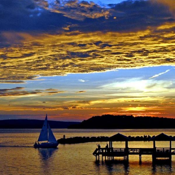 Sailboat on water at sunset with colorful sky and silhouette of pier.