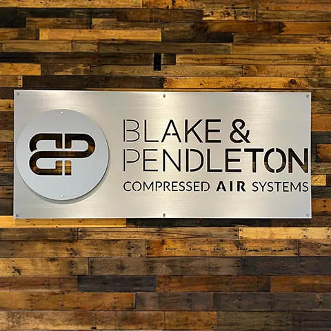 Custom metal sign for "Blake & Pendleton" with logo on wood backdrop.