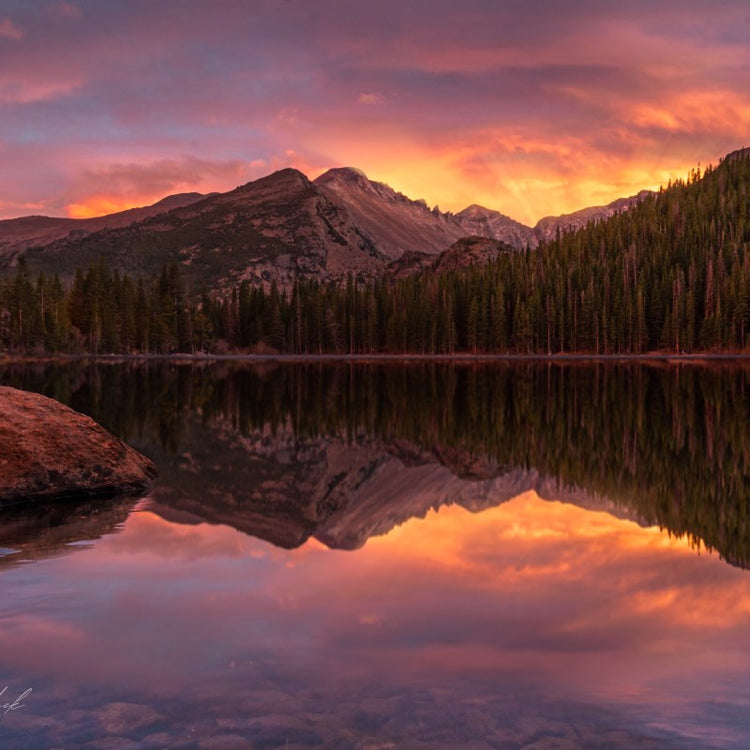 Sunset over mountain with forest reflection in calm lake.