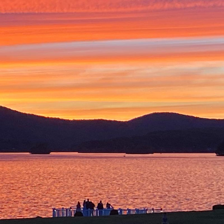 Sunset over a lake with silhouettes of people and hills.