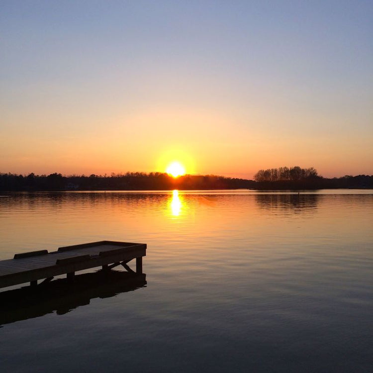 Sunset over a calm lake with a wooden dock on the left side.