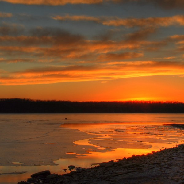 Sunset with vibrant skies reflected over partially frozen river.