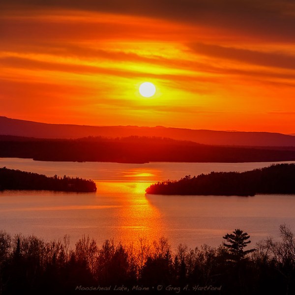 Sunset over Moosehead Lake with vibrant orange sky and sun reflecting on water.