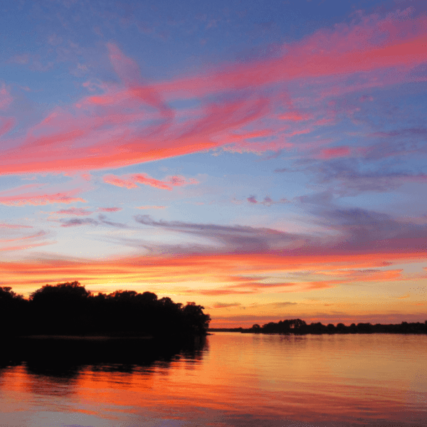 Sunset with vibrant orange and pink clouds reflecting on a lake.