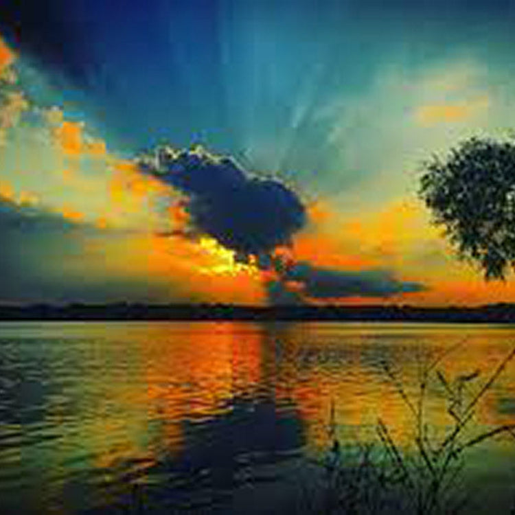 Sunset over lake with rays peeking from clouds and reflection in water.