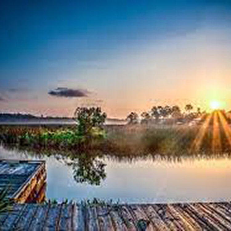 Sunrise over a calm lake with reflections and a wooden dock in the foreground.