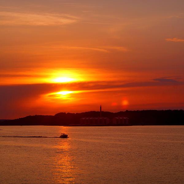 Sunset over water with boat and lighthouse silhouette.