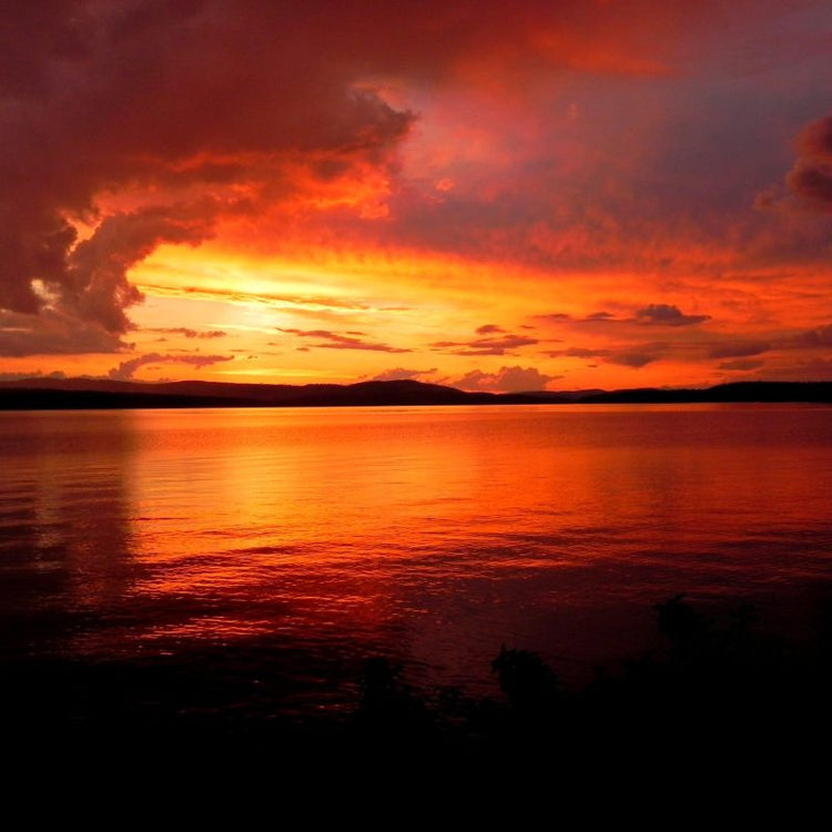 Vivid red and orange sunset over calm lake with silhouetted land.