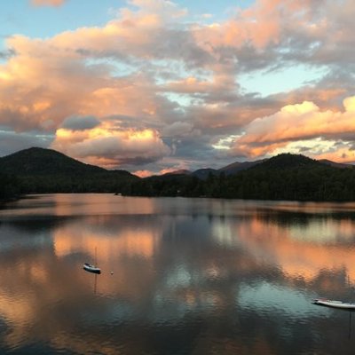 Sunset with vivid orange clouds reflected in calm lake with silhouetted hills.