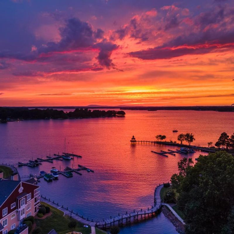 Sunset over a serene lake with a dock and boats, colorful sky reflected in the water.