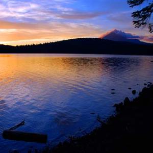 Sunset over a calm lake with silhouette of trees and mountain.