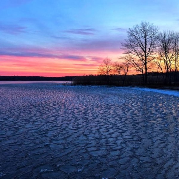 Sunset over a frozen lake with colorful sky and silhouetted trees.