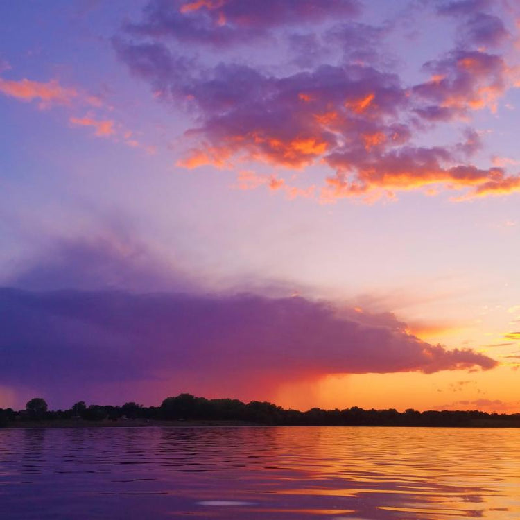 Sunset over water with purple clouds and orange sky.