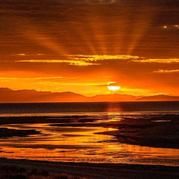 Sunset with orange skies over a reflective water body and mountain silhouette.