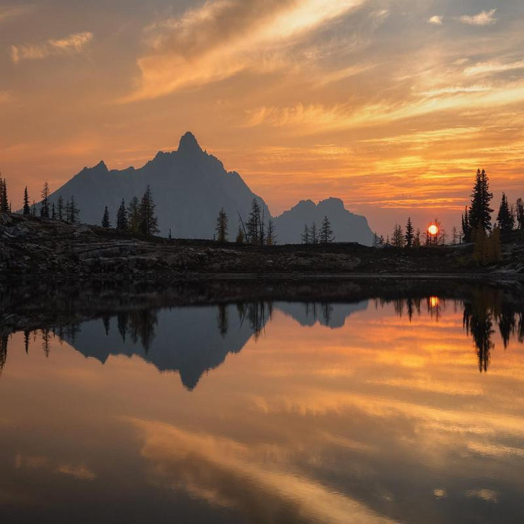 Sunset behind mountains with reflection on a tranquil lake.