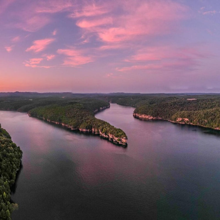 Aerial view of a winding river through lush forests at sunset.