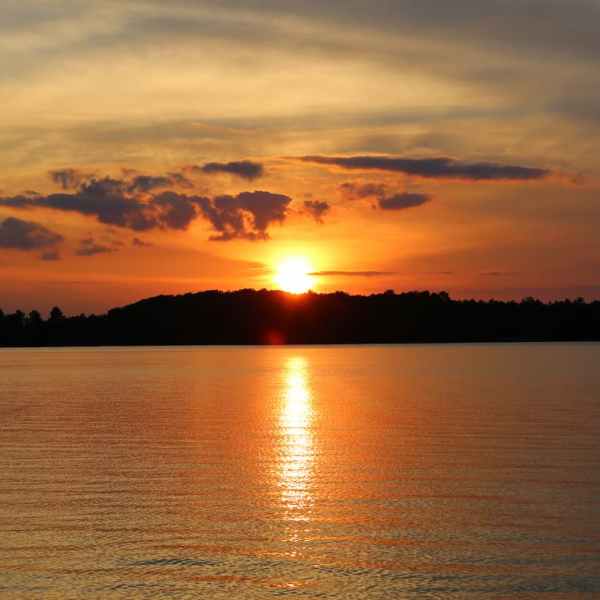 Sunset over calm lake with reflection and silhouetted trees.