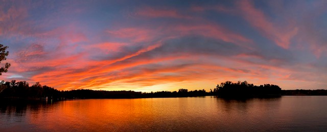 Vibrant sunset over a tranquil lake, with fiery orange and pink clouds reflecting on the water's surface.