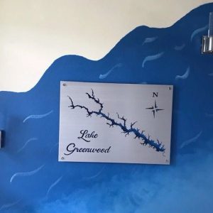 Lake Greenwood map on metal sign, mounted on blue wave-patterned wall with two modern lamps.