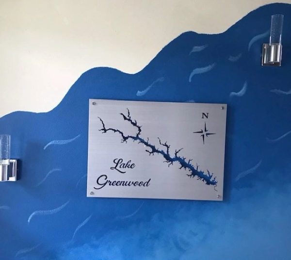 Lake Greenwood map on metal sign, mounted on blue wave-patterned wall with two modern lamps.