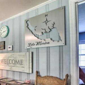 Metal sign of Lake Marion with compass rose, mounted on a striped wall above a wooden chair and decor.