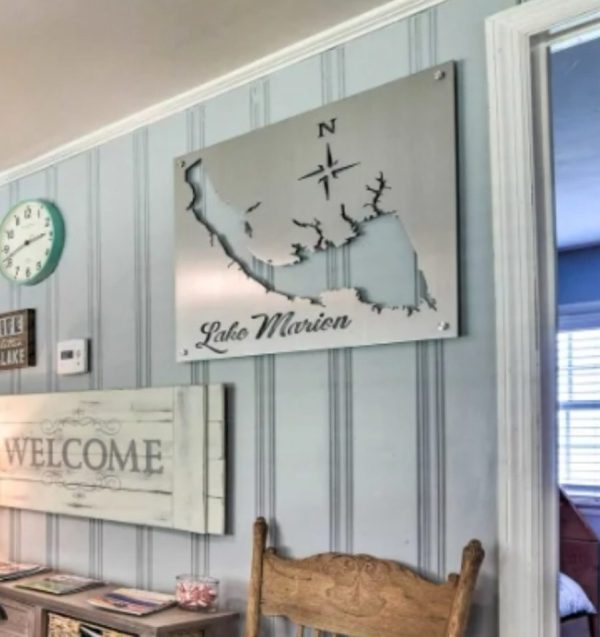 Metal sign of Lake Marion with compass rose, mounted on a striped wall above a wooden chair and decor.