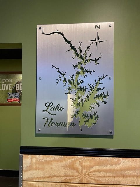 Lake Norman metal map sign with compass rose, mounted on a green wall.
