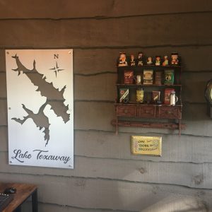 Lake Toxaway metal map with compass rose on a rustic wall, next to vintage shelf decor and an antique clock.