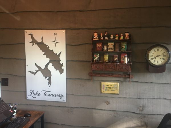 Lake Toxaway metal map with compass rose on a rustic wall, next to vintage shelf decor and an antique clock.