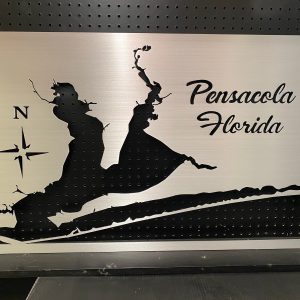 Pensacola Florida metal map with compass rose design, mounted on a black pegboard.