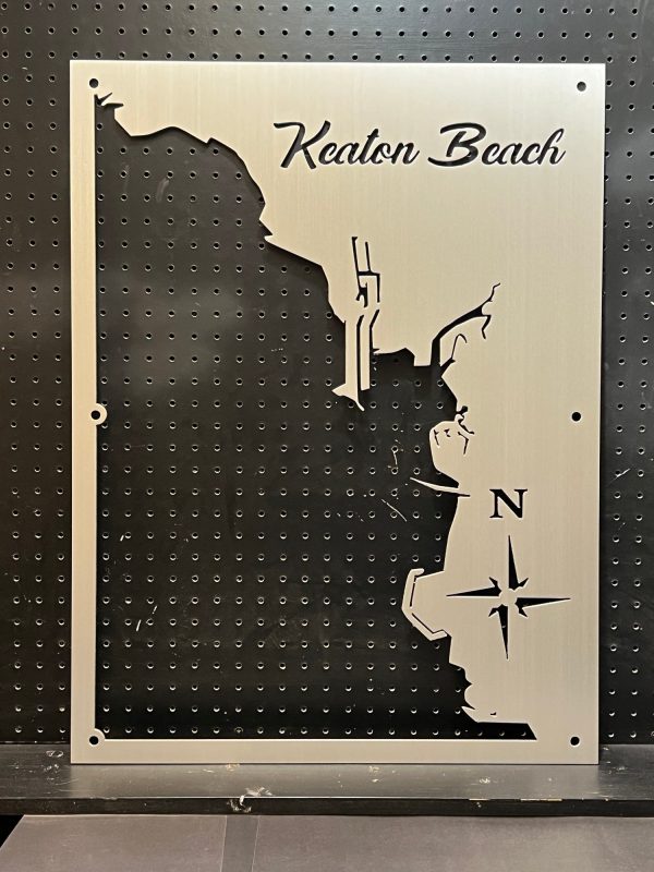 Metal map of Keaton Beach with compass design, mounted on a perforated black background.