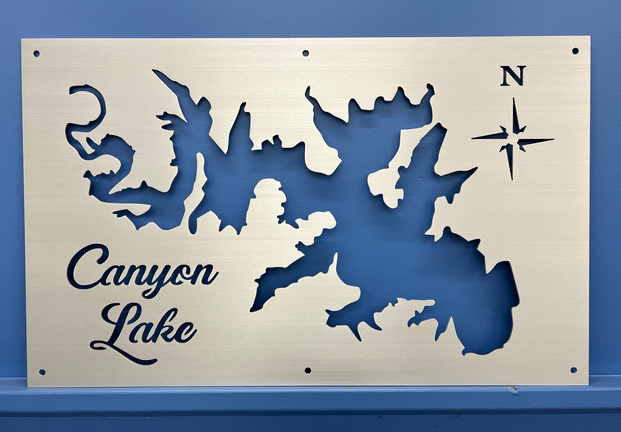 Custom metal map of Canyon Lake with cutout design and compass rose on a blue wall.