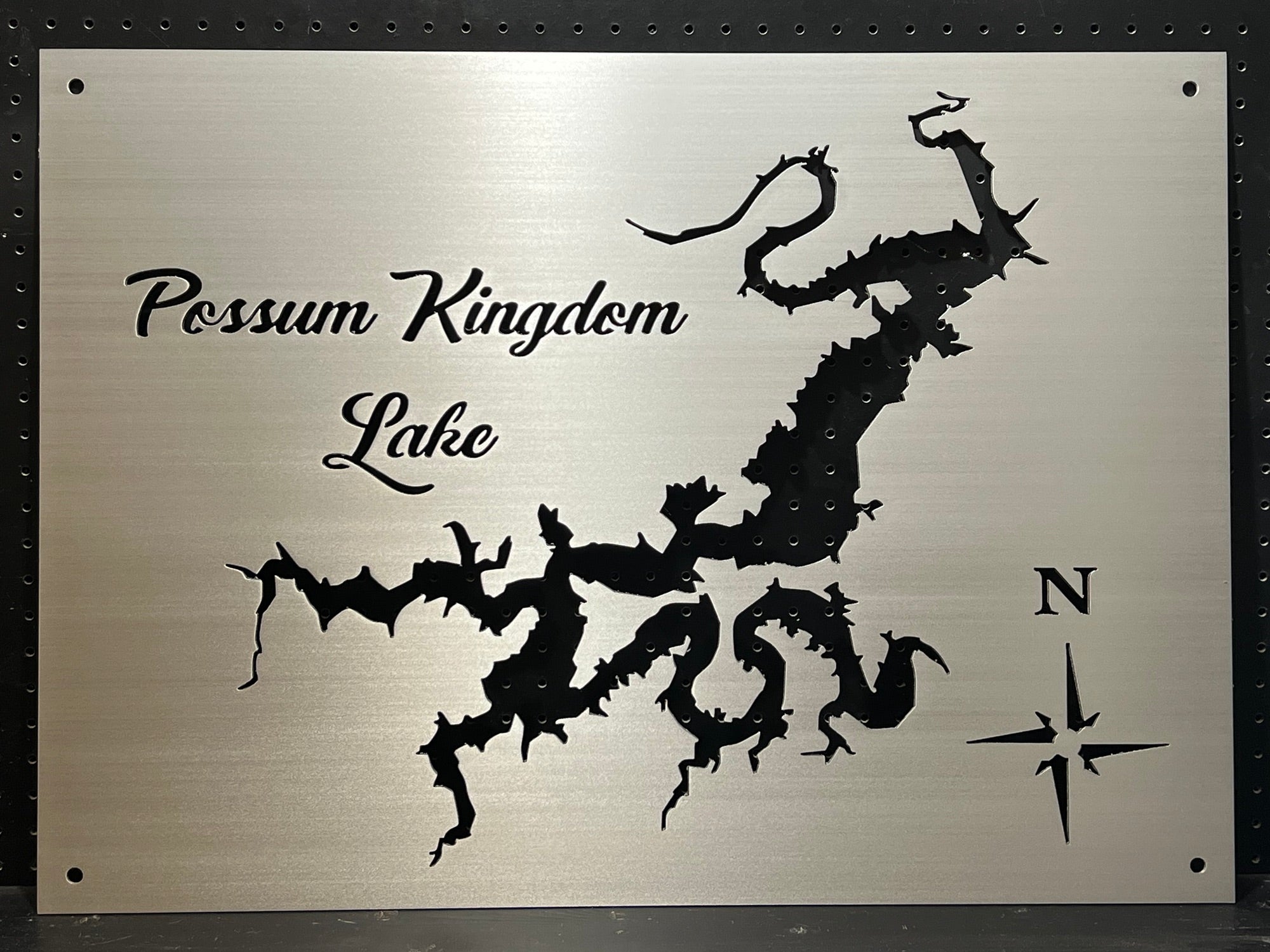 Possum Kingdom Lake metal map with compass rose, featuring intricate cutout design on brushed silver, mounted on a black pegboard.