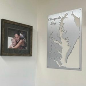 Framed family photo beside a custom metal map of Chesapeake Bay on a light-colored wall.