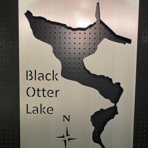 Black Otter Lake custom map sign with compass rose on perforated metal background.