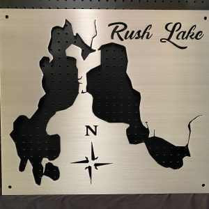 Rush Lake metal map with compass rose, mounted on a black pegboard.