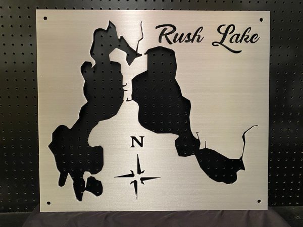 Rush Lake metal map with compass rose, mounted on a black pegboard.