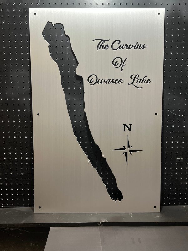 Owasco Lake metal map with "The Curvins of Owasco Lake" text and compass rose, mounted on a black pegboard.