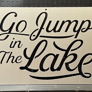 "Go Jump in The Lake" text on a custom metal sign with decorative script against a dotted background.