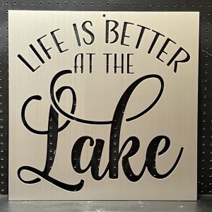 "Life is Better at the Lake" text cutout on a brushed metal sign with decorative script on perforated background.