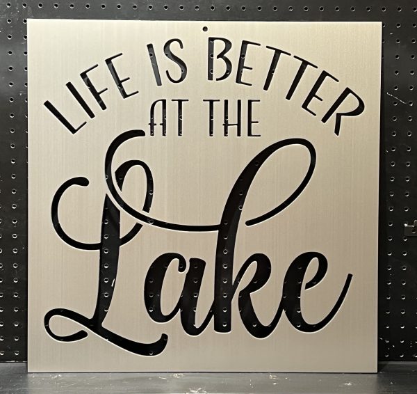 "Life is Better at the Lake" text cutout on a brushed metal sign with decorative script on perforated background.