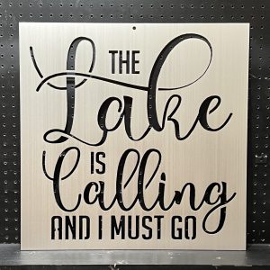 "The Lake is Calling and I Must Go" text cutout on a brushed metal sign against a perforated black background.