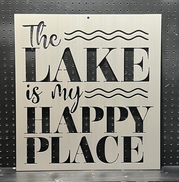 Metal sign with "The Lake is My Happy Place" text and wave design on a perforated black background.