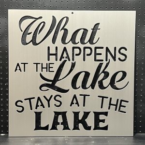 "What Happens at the Lake Stays at the Lake" text cutout on brushed metal sign against a perforated background.