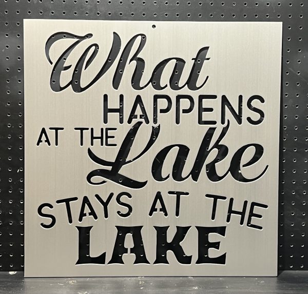 "What Happens at the Lake Stays at the Lake" text cutout on brushed metal sign against a perforated background.