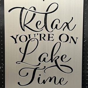 "Relax You're On Lake Time" text cutout on brushed metal sign against a perforated background.