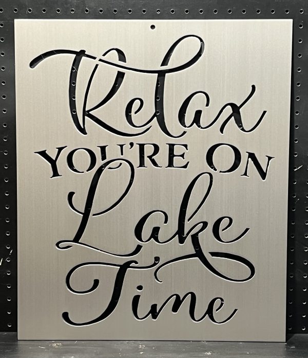 "Relax You're On Lake Time" text cutout on brushed metal sign against a perforated background.