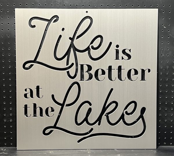 "Life is Better at the Lake" text cutout on brushed metal sign with decorative script against a perforated background.