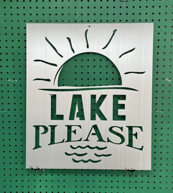 Metal sign with "Lake Please" text and sun design, mounted on a green pegboard.